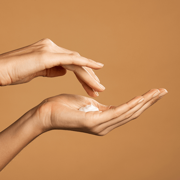 woman's hands applying organic non toxic body lotion for dry skin with neutral background